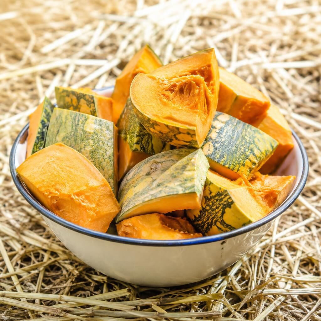 Fresh pumpkin and squash chunks in a white enamel bowl on straw
